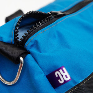 Close up image of a blue canvas duffle bag with black zip and metal D ring